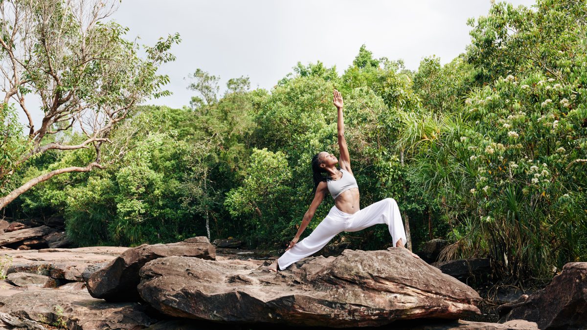 Art von Yoga Fitte Frau übt Yoga auf einem großen Felsen und macht die Kriegerpose