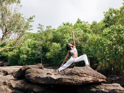 Typ av yoga Vältränad kvinna utövar yoga på en stor sten och gör krigarställning